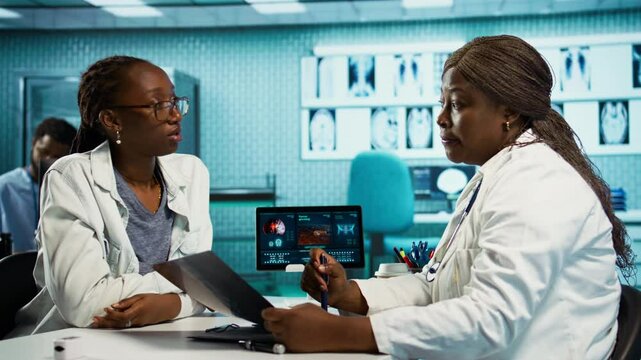 African american female doctor discussing a scary cancer diagnosis with patient, reviewing biopsy results, MRI scans and targeted treatment options like chemotherapy and immunotherapy. Camera B.