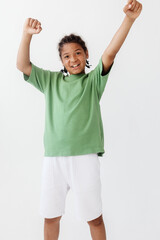 Excited young boy in green tshirt and white shorts celebrates victory with arms raised high