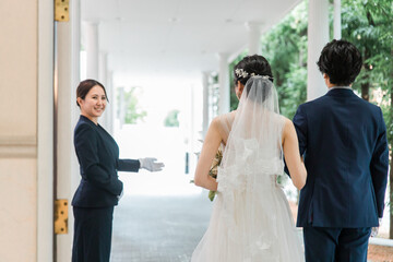 Fototapeta premium 結婚式場を案内するウェディングプランナー・ドアスタッフ・ホテリエの女性と新郎新婦（結婚式） 