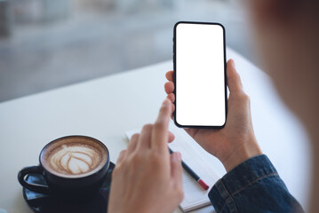 Cell phone whitw screen mockup, woman hands holding mobile phone with blank screen in coffee shop. Woman using smartphone, looking at the screen, mockup for mobile app design