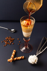 serving an italian coffee affogato in a tall glass cup on a dark blue background with coffee beans, ice cream scoop and spoon