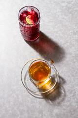 iced jamaica tea with ice and lime slice,  an a hot cup of tea  served over a grey background.