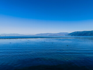 Serene lake under a vibrant blue sky.  Distant mountains create a tranquil horizon. Calm water reflects the sky.  A peaceful, idyllic landscape.