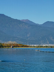 Serene lake view, autumn foliage lining the shore, mountains in the background under a clear blue sky.  Fishing structures are visible on the water.