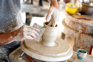 Pottery man modeling ceramic pot from clay on a potter's wheel. Closeup on male hands sculpt new utensil