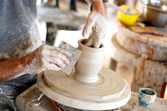 Pottery man modeling ceramic pot from clay on a potter's wheel. Closeup on male hands sculpt new utensil