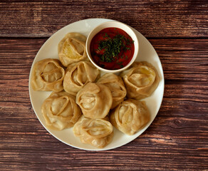 A plate of freshly steamed manti with tomato sauce on a dark wooden table.