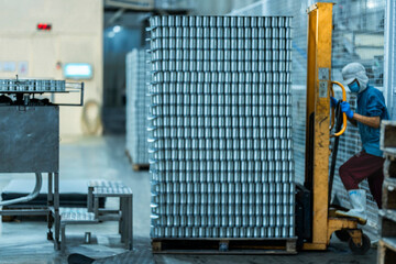 Worker operating a pallet jack to move stacked cans in a food production warehouse Focus on industrial logistics efficiency and organized manufacturing processes.