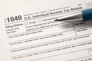Close-up view of a 1040 U.S. Individual Income Tax Return form with a pen placed on it,...