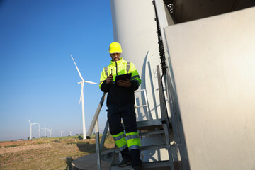 A male maintenance technician in uniform uses a talkie and a digital tablet to work on a station wind turbine. Carbon neutrality and clean energy.