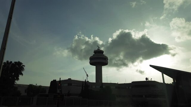 Control Tower backlighted under some clouds in a blue sky at golden hour, recorded from an airplane cockpit during the push-back maneuver. Hyperlapse.. 4K