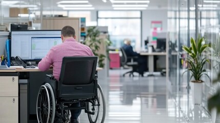 A man in a wheelchair focuses on his computer while colleagues work nearby in an office