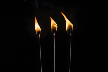 Three burning matchsticks against a black background emitting smoke.