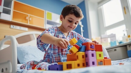 A young boy enjoys building with educational blocks in a bright hospital room while wearing pajamas