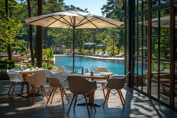 Fototapeta premium White plastic table and chairs with umbrella by the pool, surrounded by green trees on a sunny summer day, with a wooden floor and resort-style hotel swimming pool in the background.
