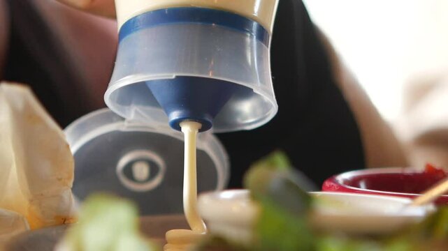 Person pouring mayo on a meal