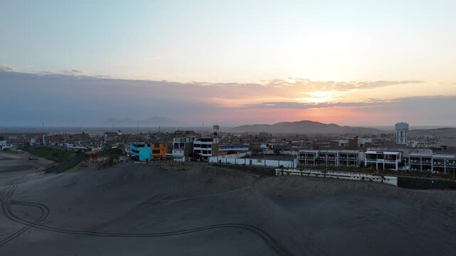 Small city build on a sand dune surrounded by desert and far away mountains during the sunrise in Peru, Puerto Malabrigo