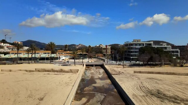 Enjoy a tranquil vista of Santa Ponsa beach in Mallorca, featuring golden sand, a gentle stream, and swaying palm trees under a bright blue sky. Perfect for relaxation and nature lovers.