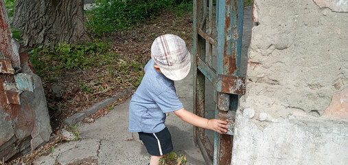 A young boy peers into a hole in a rusty metal door. The boy is wearing a gray shirt and khaki...