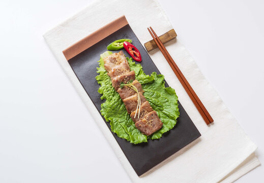 Close up and top angle view of seasoned Pork Shoulder with radish sprouts on lettuce and rectangular dish with wood chopsticks on white cloth, South Korea