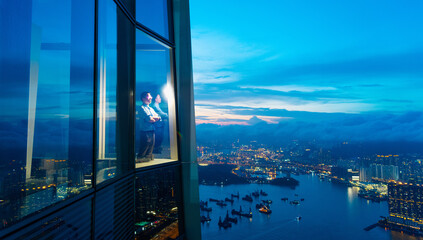 Successful businessman standing in office looking through window at big city buildings, planning new project in the evening