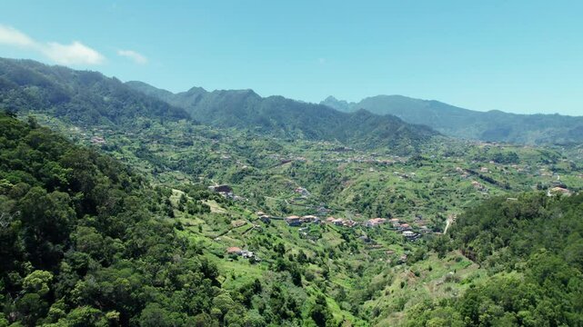 A serene 4k aerial drone video showcasing a picturesque valley nestled between lush green mountains, with a charming small village at its heart