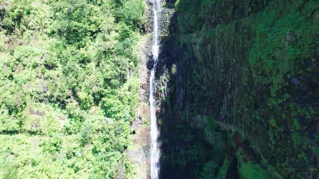 Cascading waterfall in a serene valley nestled between lush green mountains at the 25 fontes levada in Madeira, Portugal in 4k aerial drone