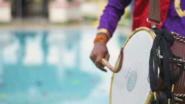 Closeup view of an Indian man playing dhol at a wedding event. Slow motion view.