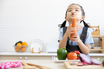 asian kid holding carrot and preparing meal in the kitchen