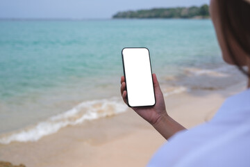 Mockup image of a woman holding mobile phone with blank desktop screen on the beach