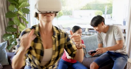 Using VR headset, woman enjoying virtual reality while family recording with smartphones - Powered by Adobe