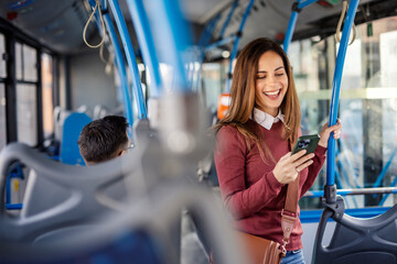 Portrait of smiling female passenger with phone in hands buying ticket online on mobile app in bus.