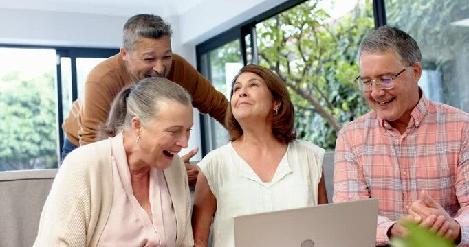 Group of senior friends talking and using laptop in living room, smiling together