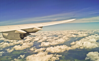 Wing of an airplane flying above the clouds on a clear sunny day. Aircraft flying high through the cumulus clouds.