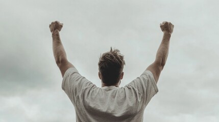 Man celebrating success, arms raised high against cloudy sky.