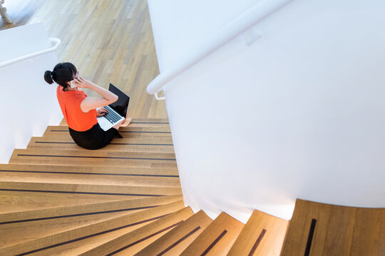 Woman sitting on staircase using smart phone and laptop
