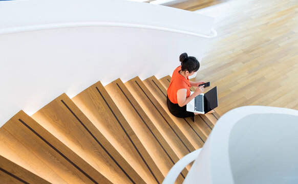 Woman sitting on staircase using smart phone and laptop - Powered by Adobe