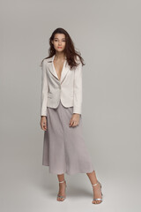 Full-body portrait of a stylish woman wearing a white blazer, neutral-toned skirt, and heels, posing confidently against a minimal studio background. Perfect for fashion and lifestyle projects.