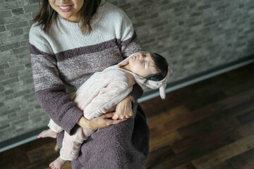 A Japanese mother in her 20s and a 6-month-old baby girl are sitting in a chair in a room. sleeping on mother's lap.