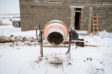 A large concrete mixer is parked in the snowcovered area in front of a building that is currently...