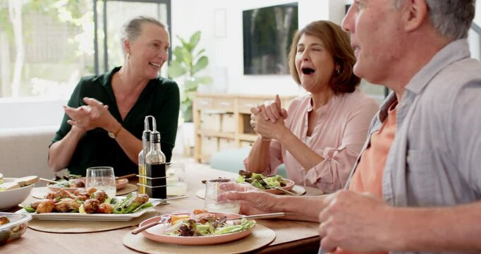 Smiling senior man enjoying meal with friends at dining table, socializing happily