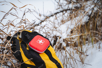 A bright red first aid kit is perched on top of a yellow and black backpack, which is almost...