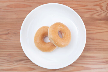 Donuts in a white porcelain dish on a pine wood table.
