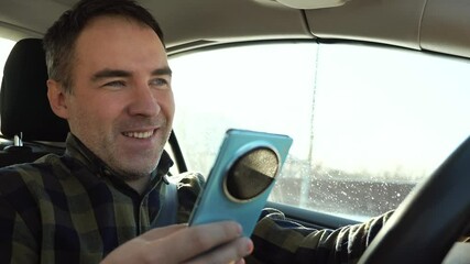 Young driver guy distracted by his phone while in front of the steering wheel, using his smartphone with one hand while driving. Risk and danger situations on the road, violating traffic rules