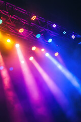 Vibrant stage lights in purple, blue, and yellow create a dynamic atmosphere during a live performance, highlighting an energetic concert setting.