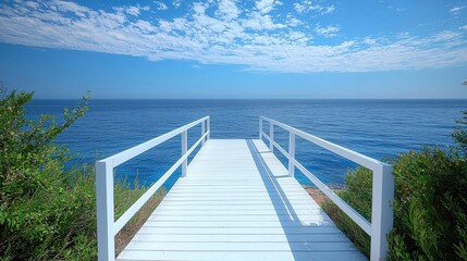 A scenic white wooden pier overlooking a tranquil blue ocean under a bright sky with scattered clouds, surrounded by lush greenery along the coast.