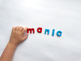Childs hand arranging colorful letter manic letters on white background