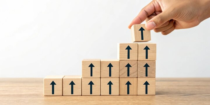 Hand placing wooden block with upward arrow on a growing stack of similar blocks symbolizing progress and growth