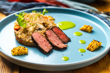 Sliced filet mignon steak with grits, mushrooms and corn served on a blue plate with a napkin and...