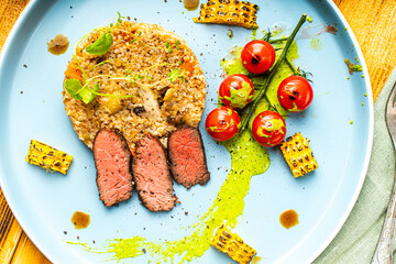 Sliced filet mignon steak with grits, cherry tomatoes, mushrooms and corn is originally served on a...